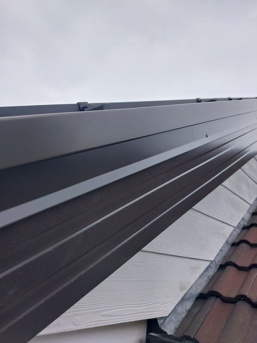 Straight new fascia and gutter line running under a tile roof