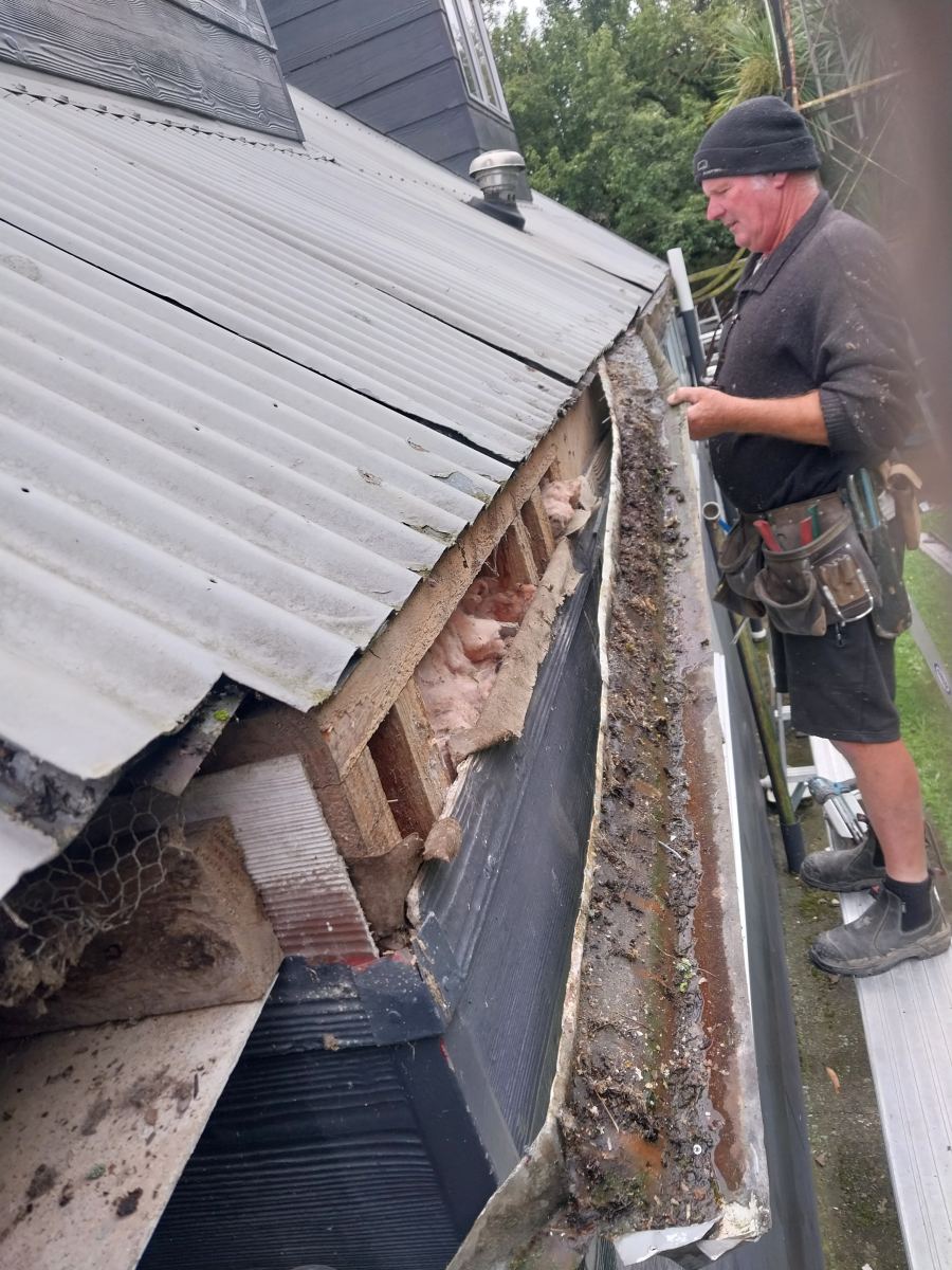 Roofer working at a corroded internal gutter that has failed at the corner