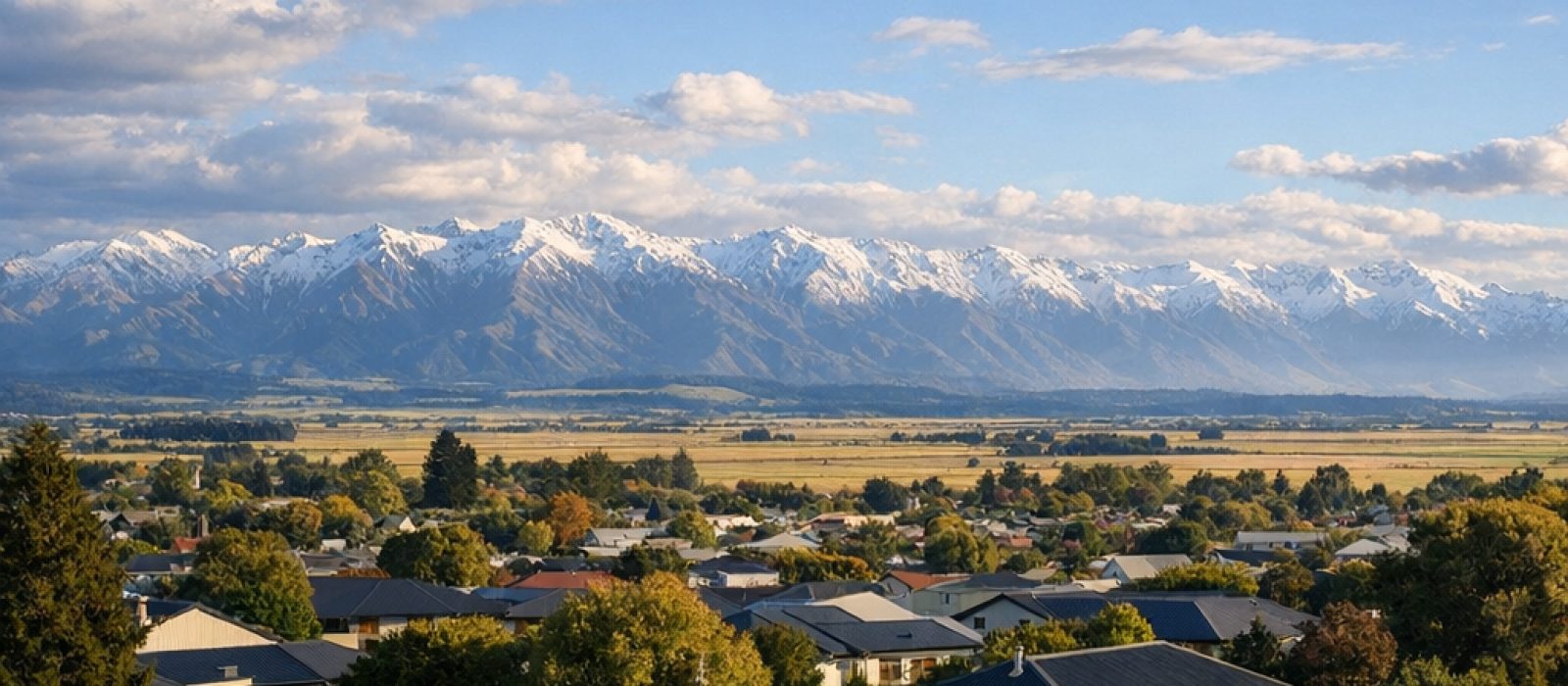 Long-run steel rooftops of a Canterbury town with the Southern Alps on the horizon