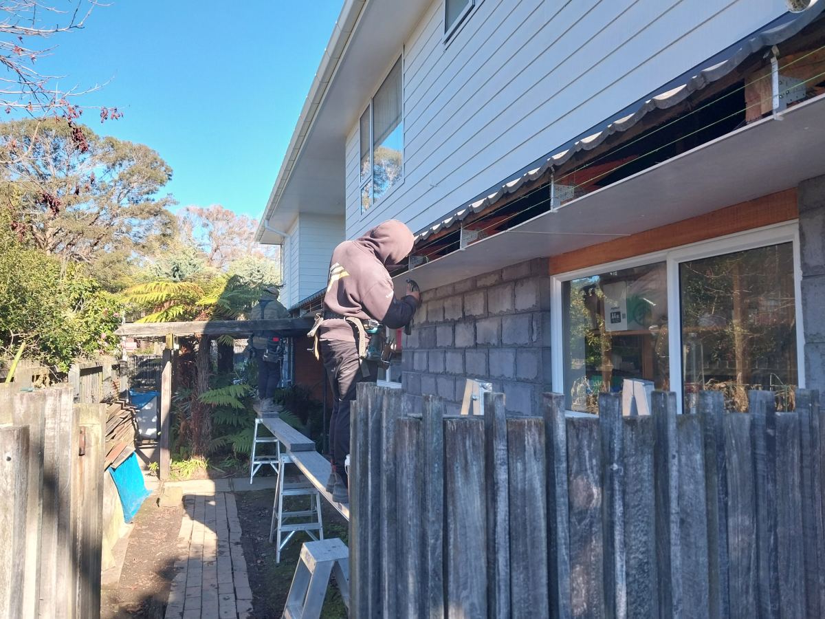 Roofer on a ladder fitting new fascia to a two-storey home