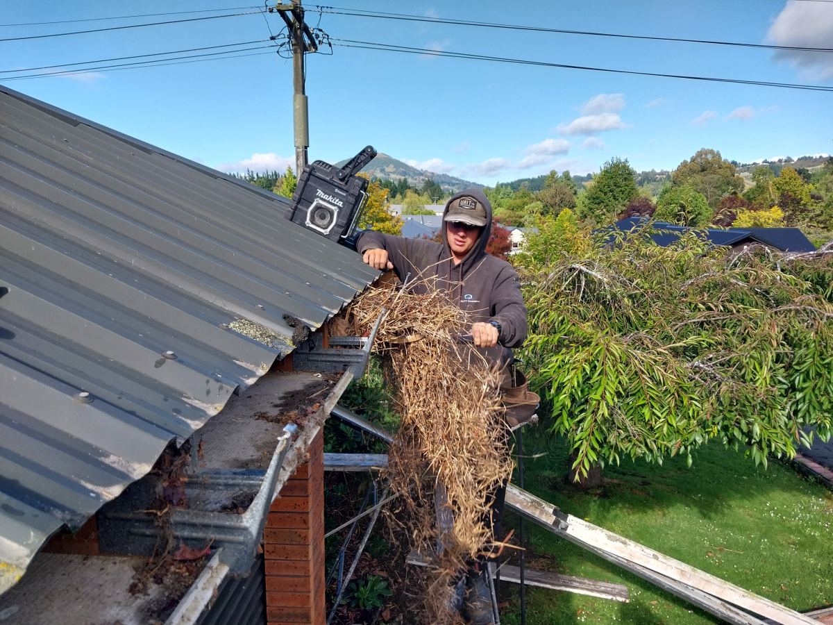 Roofer lifting a large armful of compacted debris out of a concealed gutter