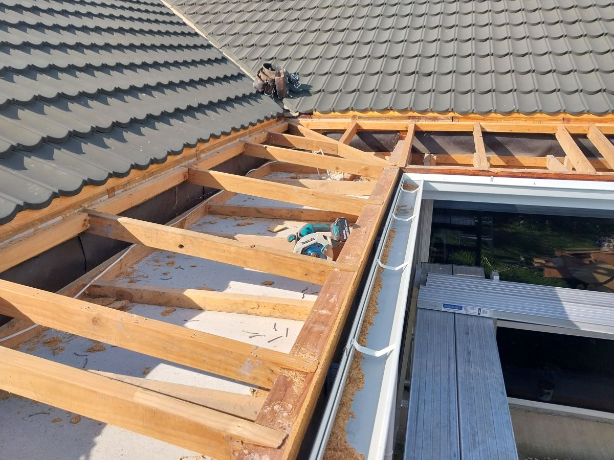 Roof section stripped back to bare timber framing beside a tile roof